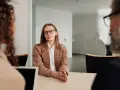 Kobieta w okularach i brązowej marynarce siedzi przy stole, przygotowując się do rozmowy kwalifikacyjnej.