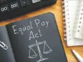 Notatnik z napisem "Equal Pay Act" i wagą sprawiedliwości symbolizuje jawność wynagrodzeń. Obok kalkulator i długopis.