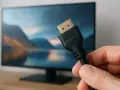 En hand håller en svart hdmi kabel 3 meter framför en datorskärm med en naturbild.