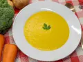 Un cremoso puré de verduras, con brócoli y zanahorias frescos al lado, listo para disfrutar.