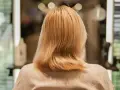 Blond włosy po zabiegu farba demi permanentna, delikatnie pofalowane, w tle rozmyte światła salonu fryzjerskiego.