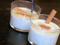 Deux verres de riz au lait crémeux, saupoudrés de cannelle. Un bâton de cannelle décore l'un des desserts, parfait pour une recette de riz au lait.