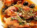 Coniglio alla ligure succulento, con olive nere e erbe aromatiche, servito in un piatto bianco.