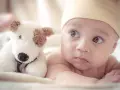 Urocze roczne dziecko w żółtej czapeczce leży obok pluszowego pieska, zastanawiając się, ile jeszcze drzemek czeka go dzisiaj.