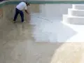 Hombre pintando una piscina de cemento con rodillo. La mitad de la piscina ya está pintada de blanco.