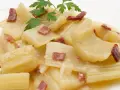 Cardo a la navarra, un plato tradicional con trozos tiernos de cardo en una cremosa salsa, adornado con trocitos de jamón y perejil fresco.