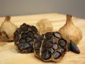 Ajos negros enteros y cortados, mostrando sus dientes oscuros y arrugados. Descubre las increíbles ajo negro propiedades.