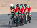 Équipe cycliste marocaine en tenue rouge et verte, concentrée sur la course. Ils roulent en peloton, tels des pur sang arabes noirs, sur un parcours désertique.