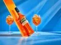 Aperol, znany z orzeźwiającego smaku, ma 11% alkoholu. Na zdjęciu butelka i dwa drinki z pomarańczą.