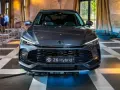 Szary MG ZS Hybrid+ prezentuje się elegancko na tle wnętrza z zasłonami i krzesłami.