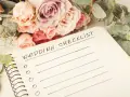Bukiet róż i eukaliptusa obok notatnika z napisem "Wedding Checklist". Planowanie przebiegu wesela zaczyna się od listy zadań.