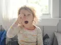 Małe dziecko zaspane, przeciera oko i ziewa, sugerując poranny nieświeży oddech.