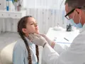 Lekarz bada szyję dziewczynki, by wykluczyć niedoczynność tarczycy u dziecka a zachowanie.