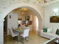 Un elegante soggiorno con un **arco in pietra moderno** che separa la zona pranzo dalla cucina. Divano bianco, quadri e lampadario di cristallo.