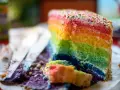 Ein Stück bunter **Regenbogen Kuchen** mit bunten Streuseln, das auf einem Teller liegt. Daneben liegen Krümel und ein Messer.