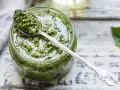 Un vasetto di pesto genovese fatto in casa con frullatore, pronto per essere gustato. Un cucchiaino d'argento raccoglie un po' di questa delizia verde.