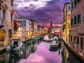 Un canale di Venezia al tramonto, con barche ormeggiate e riflessi viola sull'acqua. Un'atmosfera magica che ricorda i piombi di Venezia.
