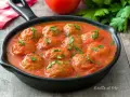 Polpette di lenticchie in salsa di pomodoro, guarnite con prezzemolo fresco, servite in una padella nera su un tavolo di legno.