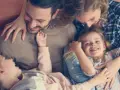 Glückliche Familie kuschelt auf dem Sofa. Zwei Elternteile umarmen ihre zwei Kinder, die sich an sie schmiegen.