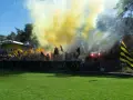 Fani Nielby Wągrowiec świętują, odpalając race i machając flagami. Żółto-czarne barwy dominują na trybunach.