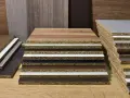 Campioni di laminato plastico con diverse finiture effetto legno e colori solidi, impilati su un piano di legno.