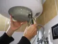Mani che effettuano la manutenzione dello scaldabagno elettrico, avvitando una vite con un cacciavite.