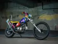 Kolorowy motocykl po malowaniu, z żółtym siedzeniem i niebieskim bakiem ozdobionym różowymi wzorami.