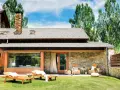 Fachadas de casas de pueblo modernas con piedra y madera, jardín con tumbonas y zona de estar exterior.