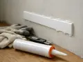 Narzędzia do montażu listwy przypodłogowej: rękawice, nóż, pistolet z masą uszczelniającą. Czekamy aż masa schnie, mamut by się nie powstydził cierpliwością.