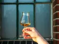 Ein Glas bernsteinfarbener Whisky wird vor einem Fenster gehalten. Der Alkoholgehalt ist bei dieser Verkostung entscheidend.