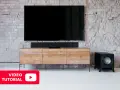 Schwarzer Subwoofer neben einem TV-Möbel. Hier erfahren Sie mehr über den subwoofer anschluss.