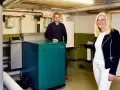 Mann und Frau stehen neben einem grünen Nano BHKW-Gerät in einem Heizungsraum.
