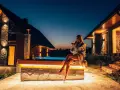 Kobieta w szlafroku z drinkiem siedzi przy jacuzzi przed górskim domkiem.