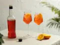 Dwa orzeźwiające drinki aperol z colą, ozdobione plasterkami pomarańczy, stoją obok butelki aperolu.