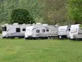 Rząd przyczep kempingowych na zielonej trawie, w tle las. Idealne miejsce na camping Górna Wetlinka.