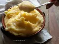 Un cucchiaio solleva una porzione filante di polenta concia valdostana, calda e cremosa, in una ciotola di terracotta.