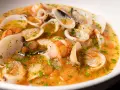 Sopa de mariscos con gambas, calamares y almejas en un caldo dorado con perejil.