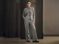 Elegancka kobieta w szarym garniturze, idealnym na wesele. Spodnie z szerokimi nogawkami i marynarka tworzą stylowy zestaw.