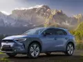Niebieski Subaru Solterra stoi nad jeziorem z górami w tle.