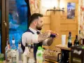 Barman na wesele cena: profesjonalista miesza drinki za barem, otoczony butelkami alkoholu i dekoracjami.