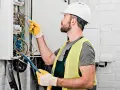 Elektryk w kasku i kamizelce odblaskowej pracuje przy skrzynce z przewodami. Sprawdź nasz cennik usług elektrycznych!