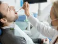 Pacjent u dentysty, zastanawia się, ile kosztuje wizyta u dentysty prywatnie. Lekarz bada jego zęby.