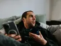 Mann liegt auf Sofa, hält Tasse und Handy. Mögliche Bewegungsmangel Symptome wie Müdigkeit und Lethargie werden angedeutet.