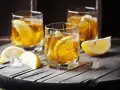 Metaxa orange z czym pić? Idealnie z lodem i plasterkiem cytryny. Trzy szklanki złocistego trunku na drewnianym blacie.