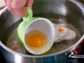 Ein rohes Ei wird aus einer grünen Tasse in kochendes Wasser gegossen, um verlorene Eier zuzubereiten.