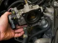 Mano che tiene il corpo farfallato, possibile causa di problemi al motore a metano.
