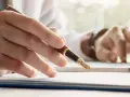 Person schreibt mit Füllfederhalter auf Dokumenten, während er am Laptop arbeitet. Ein gutes Beispiel für einen Praktikumsbericht.