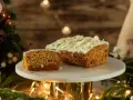 Pyszny, wilgotny naked cake marchewkowy z kremem i wiórkami białej czekolady, udekorowany świątecznymi światełkami i gałązkami choinki.
