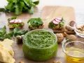 Zielone pesto w misce, obok składniki: ser, orzechy, cytryna, czosnek, oliwa.