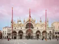 La Basilica di San Marco a Venezia, con il suo cielo rosa al tramonto e la piazza animata da turisti.